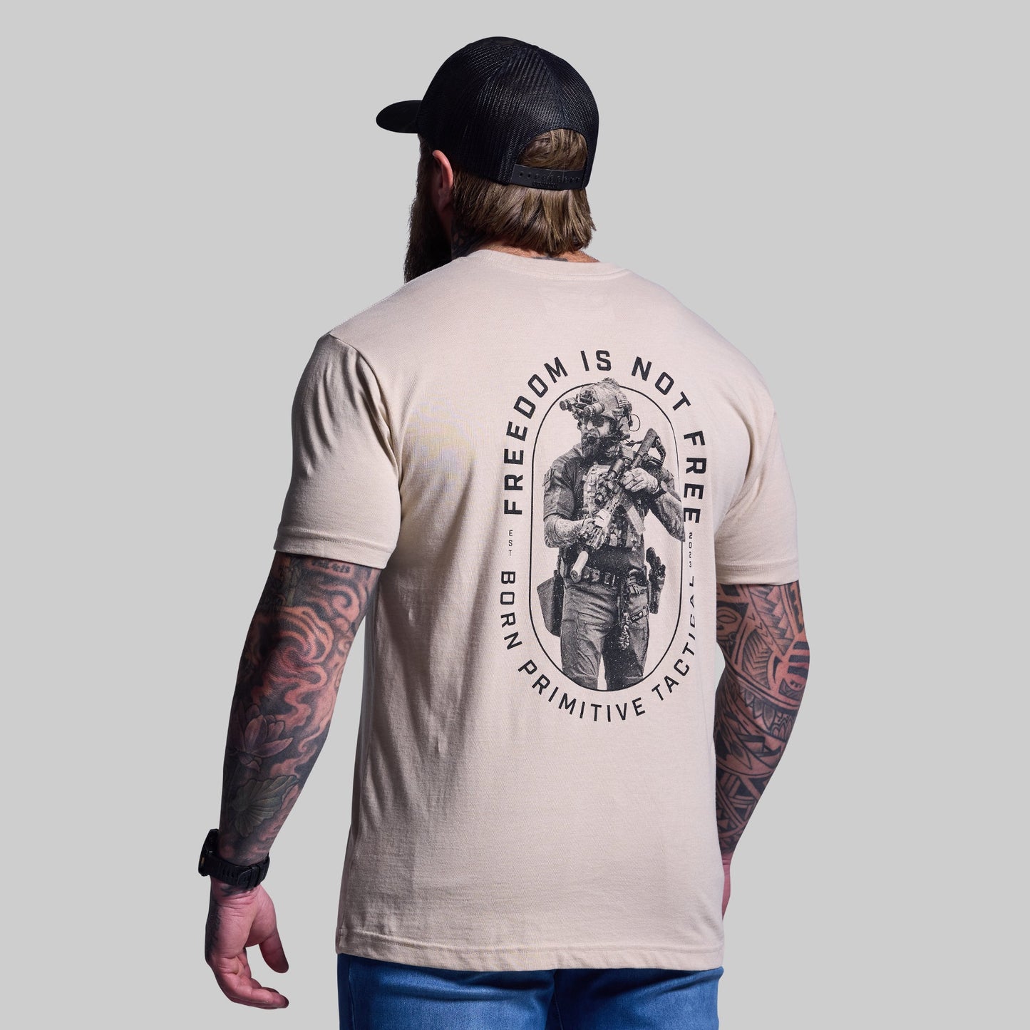 Man wearing a beige t-shirt with a graphic design and text on the back, standing against a plain background.