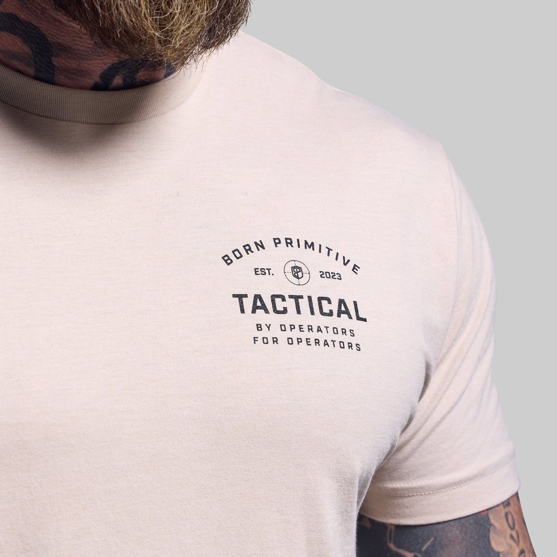 Person wearing a light-colored t-shirt with 'Born Primitive Tactical' logo on a gray background