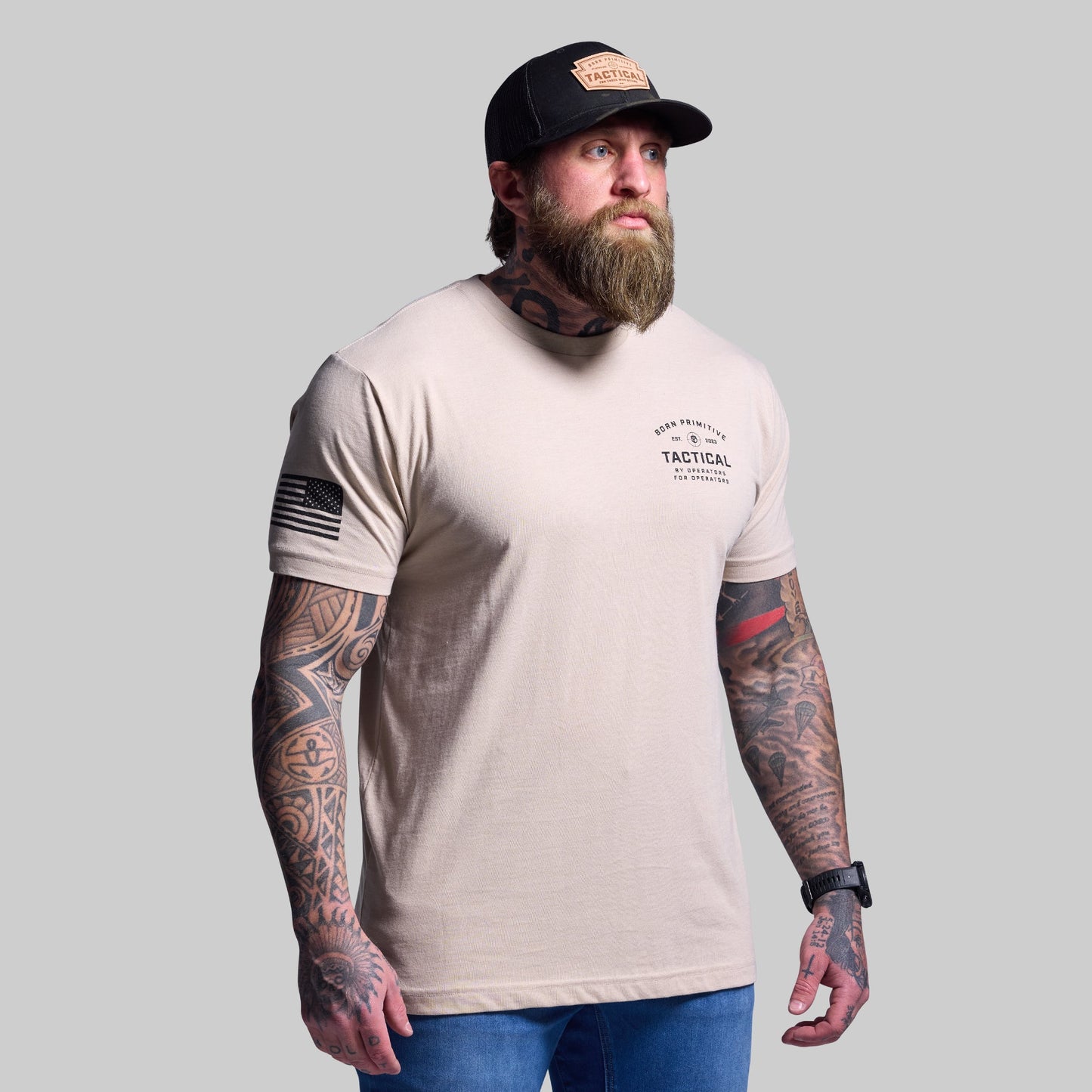 Man wearing a beige t-shirt with tactical design and a cap on a gray background