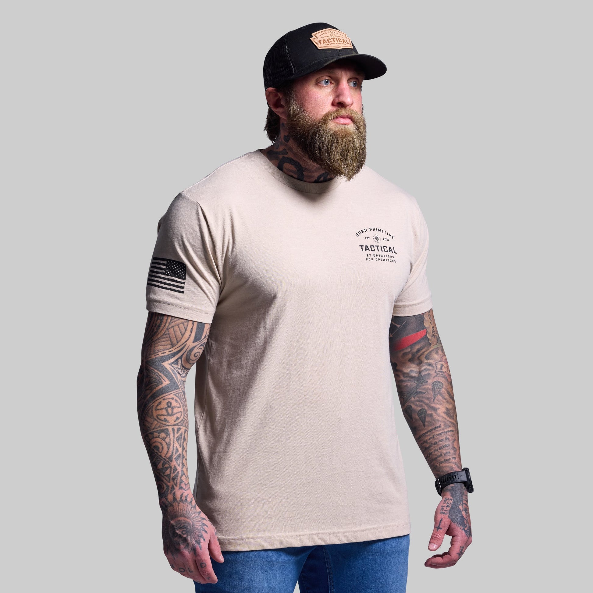 Man wearing a beige t-shirt with tactical design and a cap on a gray background
