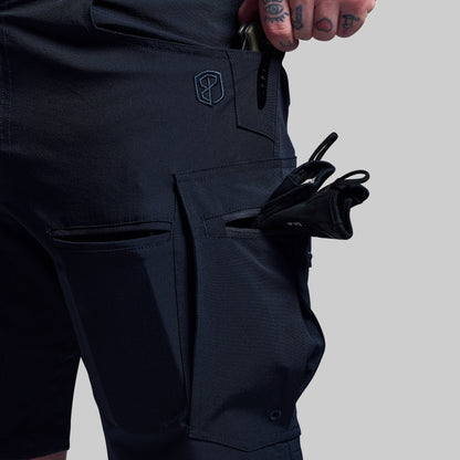Person wearing dark blue shorts with a visible brand logo with multiple objects in pockets, on a light gray background