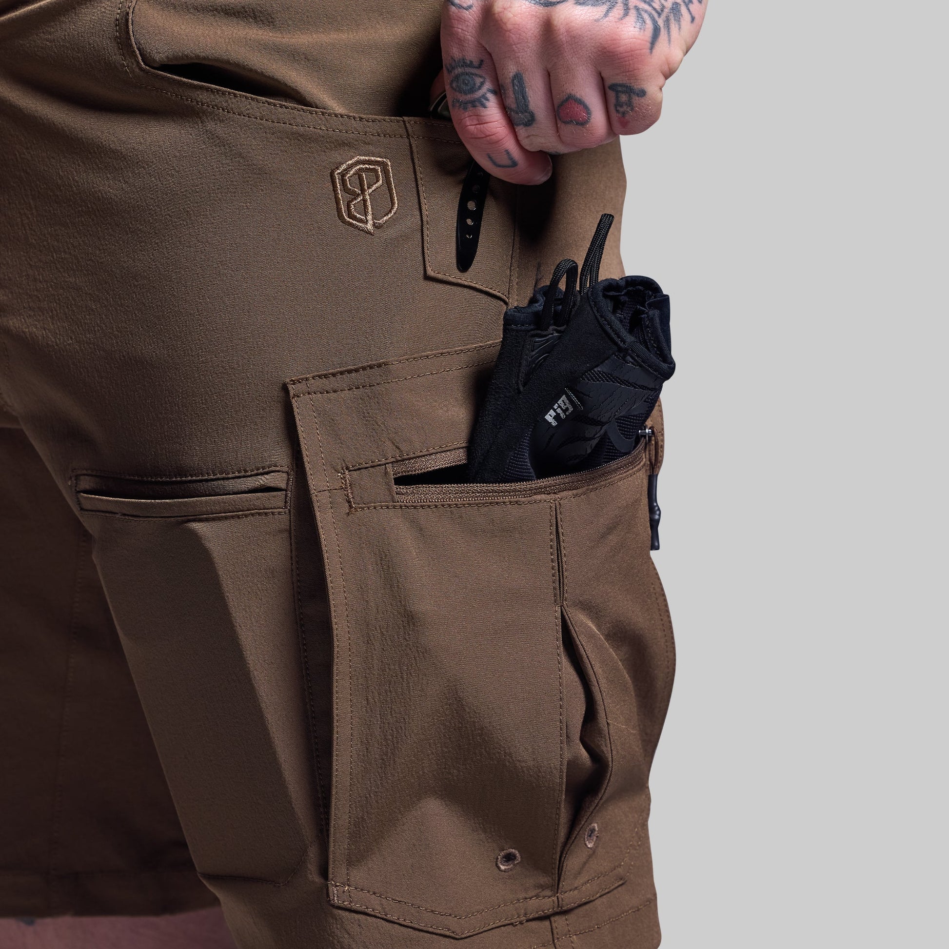 Brown shorts with a pocket containing a black item on a gray background