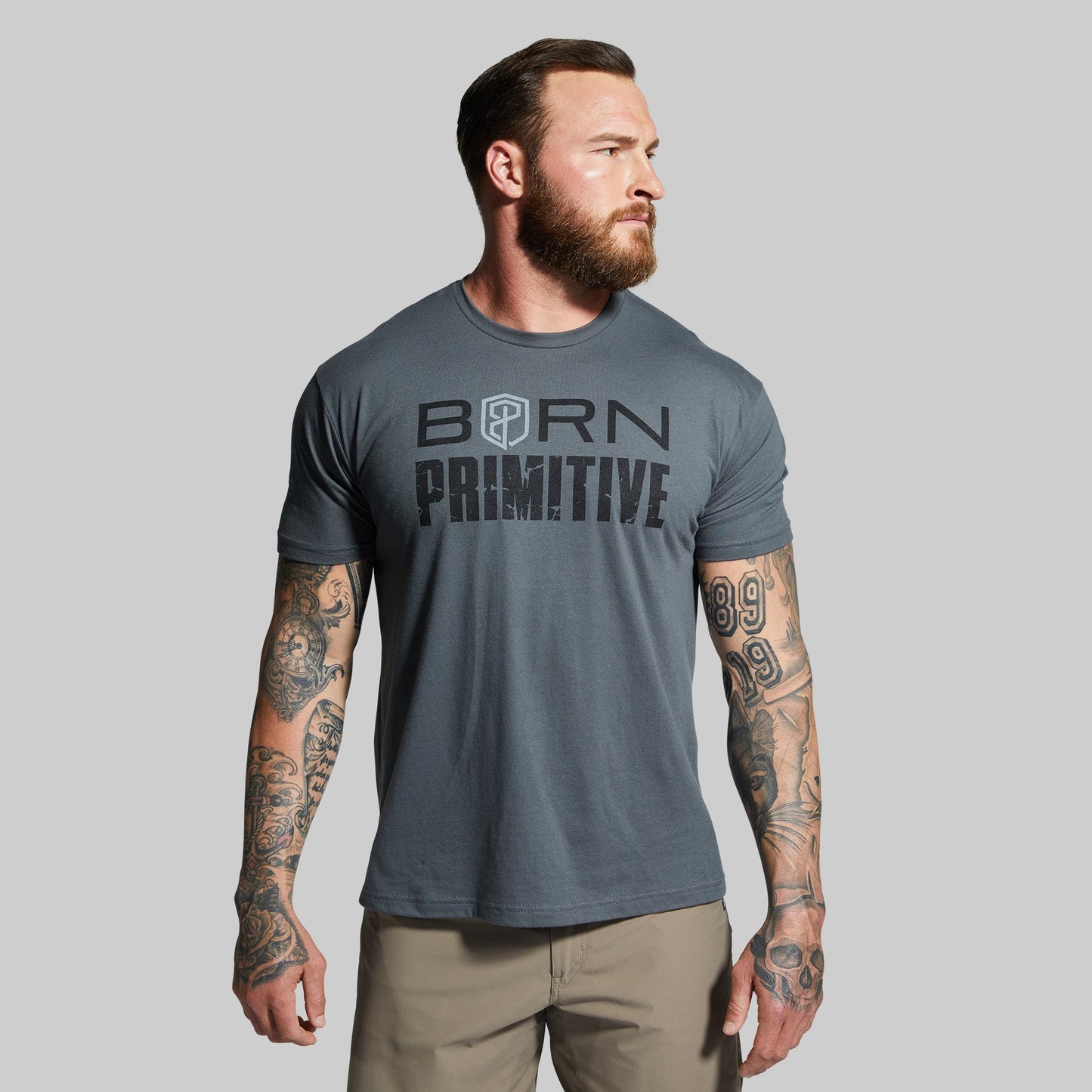 Man wearing a gray t-shirt with 'Born Primitive' text on a plain background