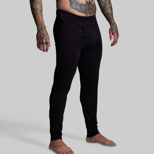 Person wearing black base layer pants on a plain background