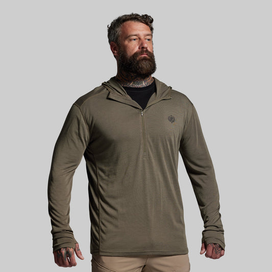 Man wearing a green hooded base layer on a gray background