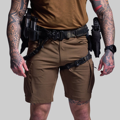 Person wearing brown tactical shorts with tattoos on arms and legs, holding holstered weapons.
