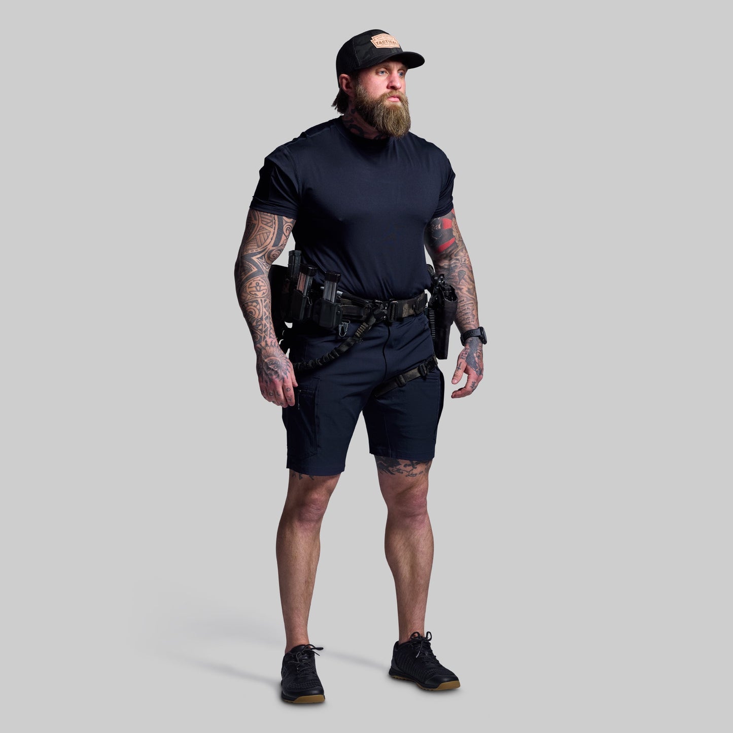 Man wearing a dark blue t-shirt, shorts, and cap on a gray background