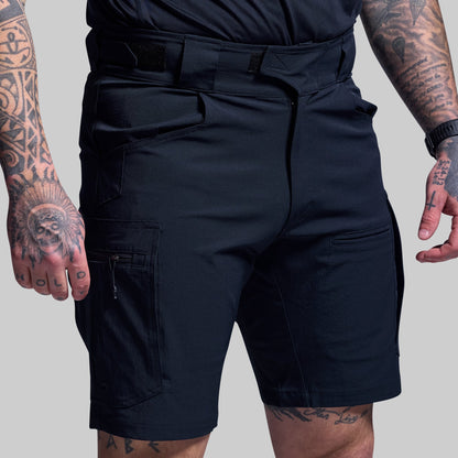 Person wearing blue tactical shorts with tattoos on arms and legs against a gray background