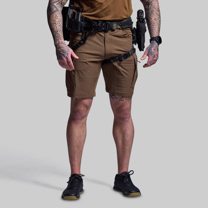 Person wearing brown tactical shorts with visible tattoos on arms and legs, on a plain background