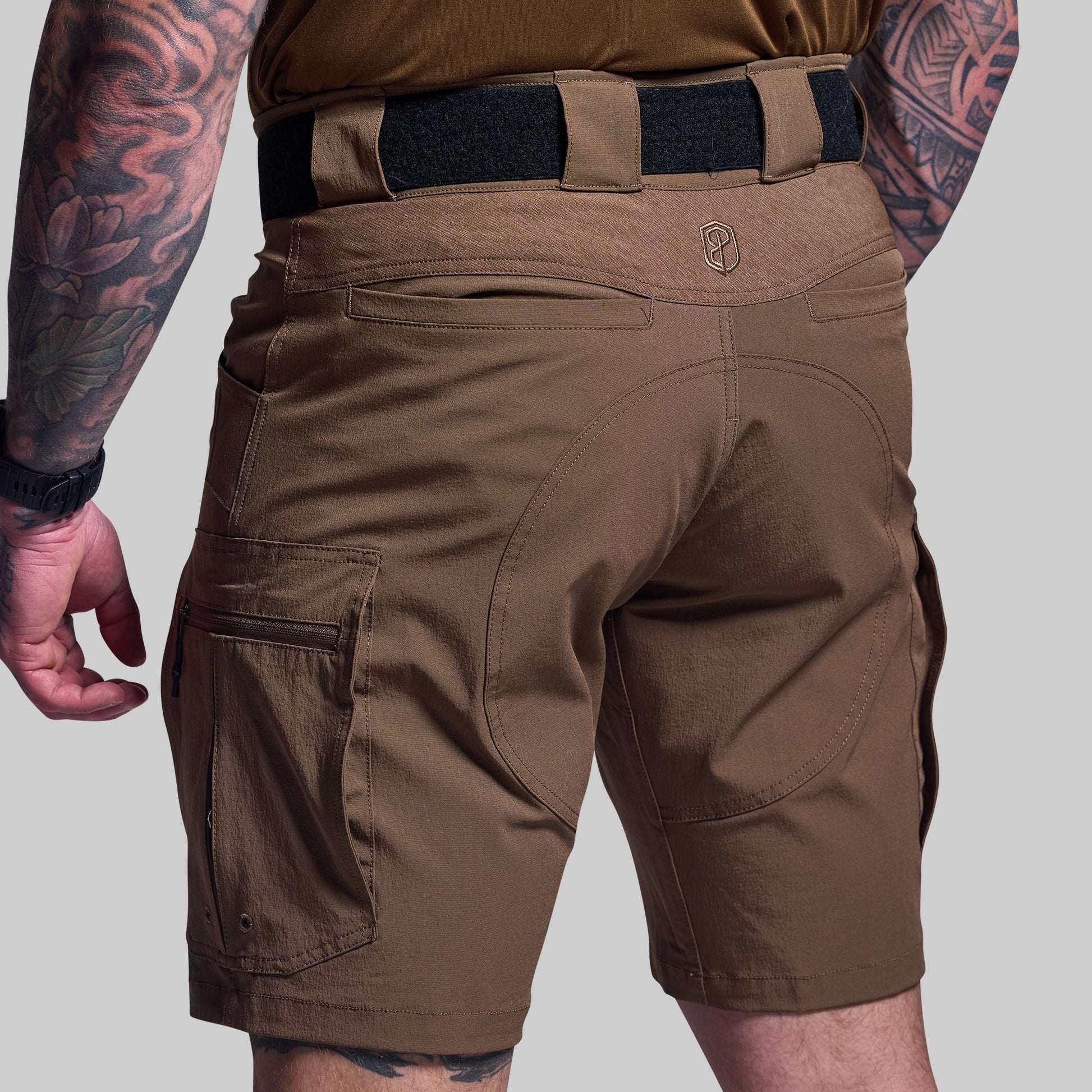Brown shorts worn by a person with tattoos on a gray background