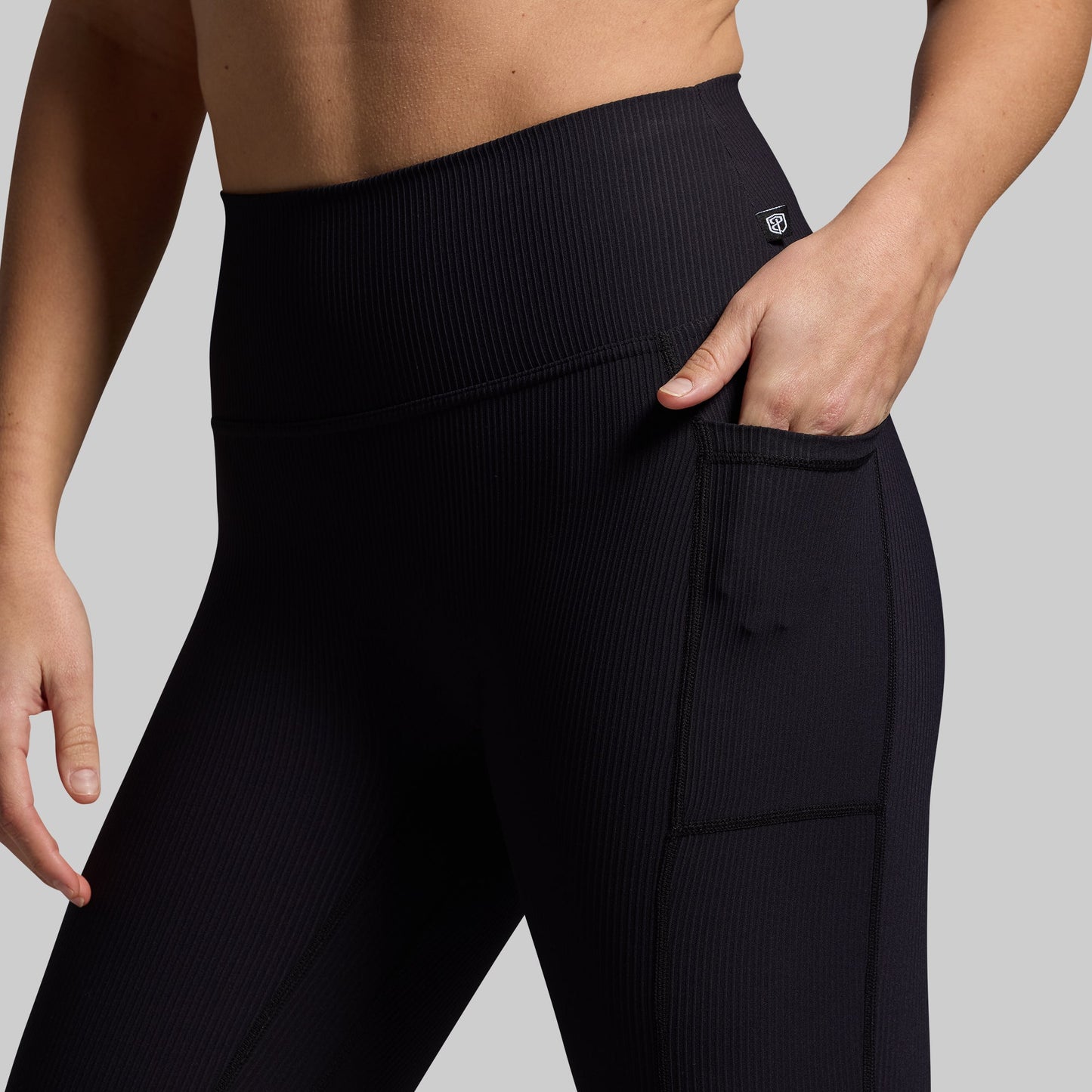 Black leggings worn by a person with hand in pocket on a gray background
