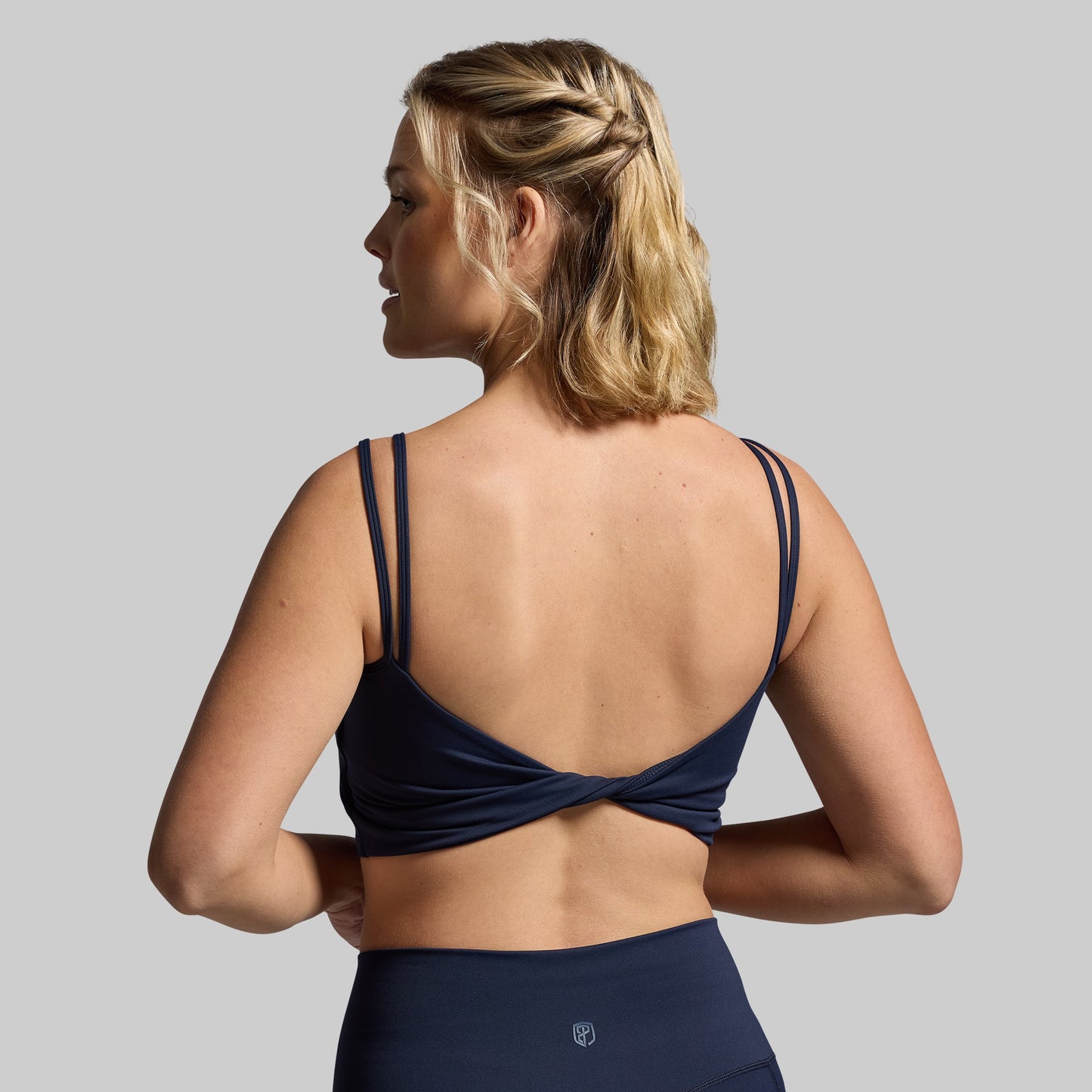 A navy sports bra with a unique twisted back design, viewed from the back.