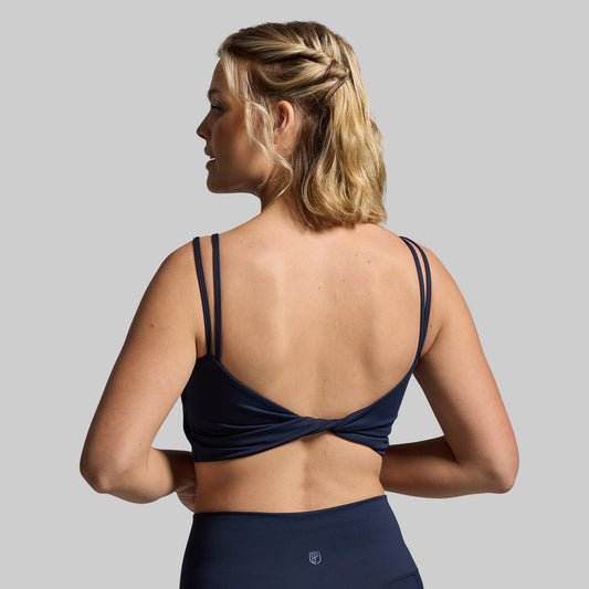 A navy sports bra with a unique twisted back design, viewed from the back.