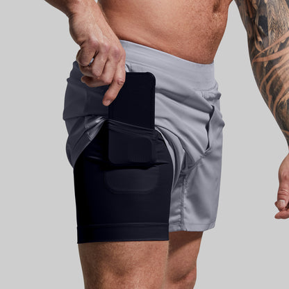 Person wearing gray shorts with a black compression liner pocket on a plain background