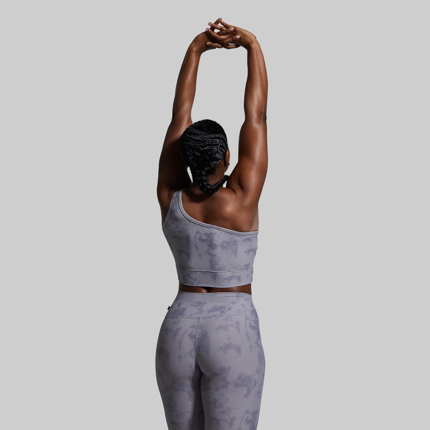 Person wearing a gray patterned athletic outfit stretching against a light gray background
