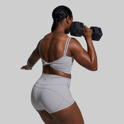 Person lifting a dumbbell in gray sports bra and shorts set on a plain background