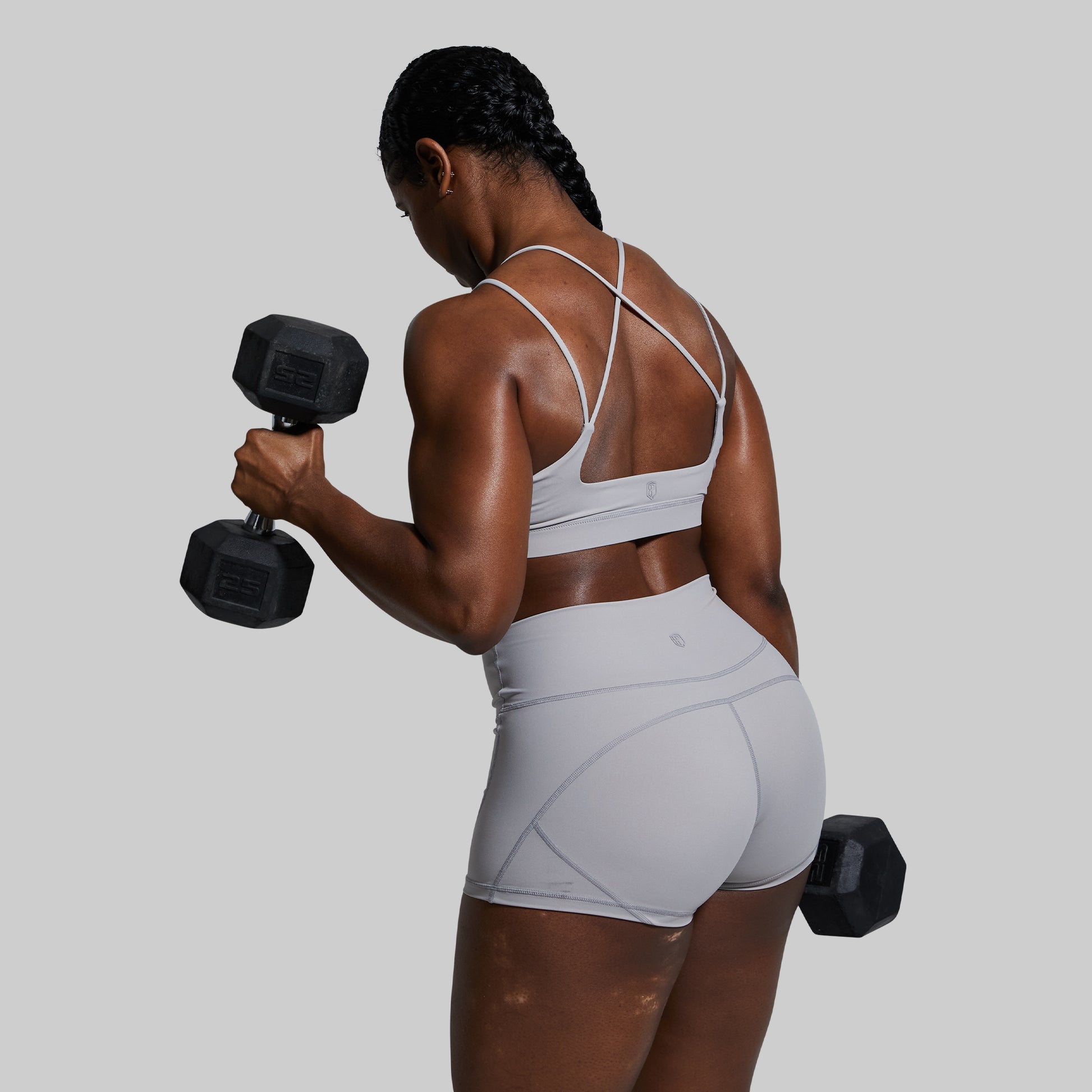 Woman in athletic wear holding dumbbells against a gray background