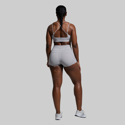 Person wearing a gray sports bra and shorts set on a plain background