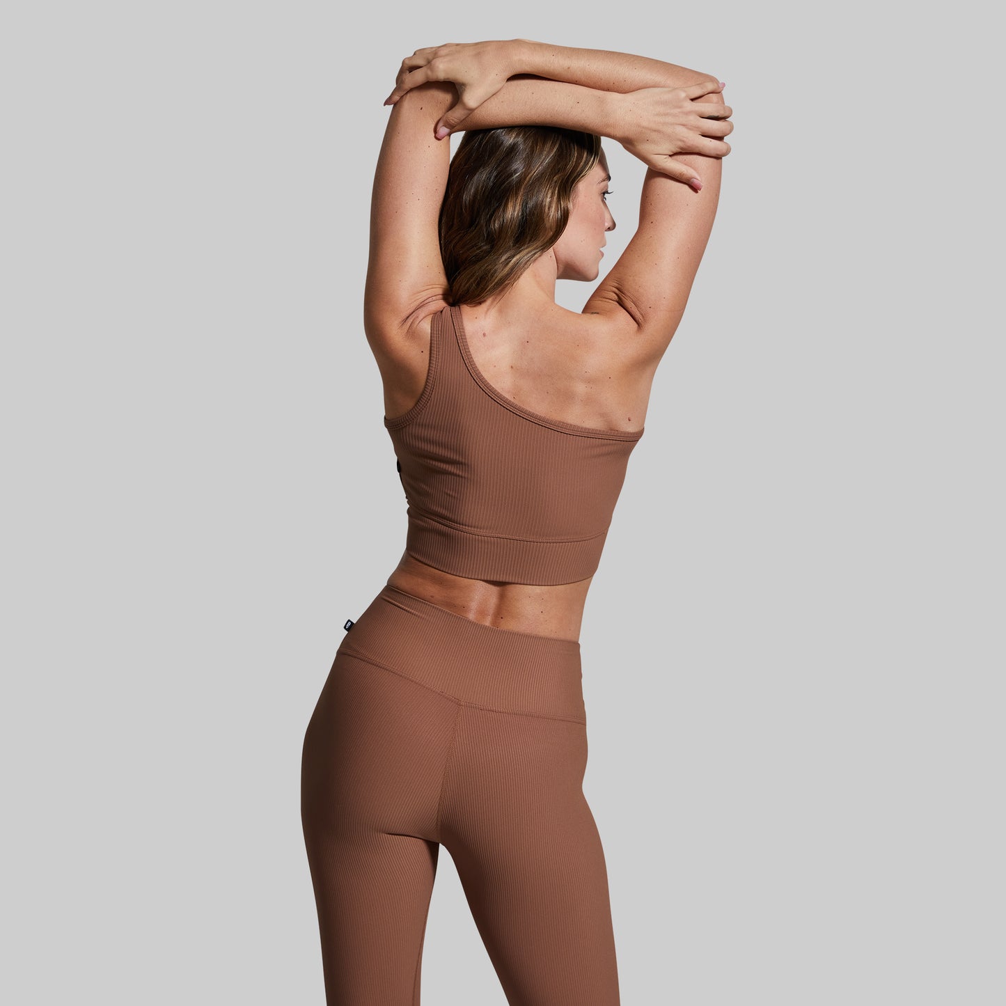 Woman wearing a brown athletic outfit stretching against a plain background
