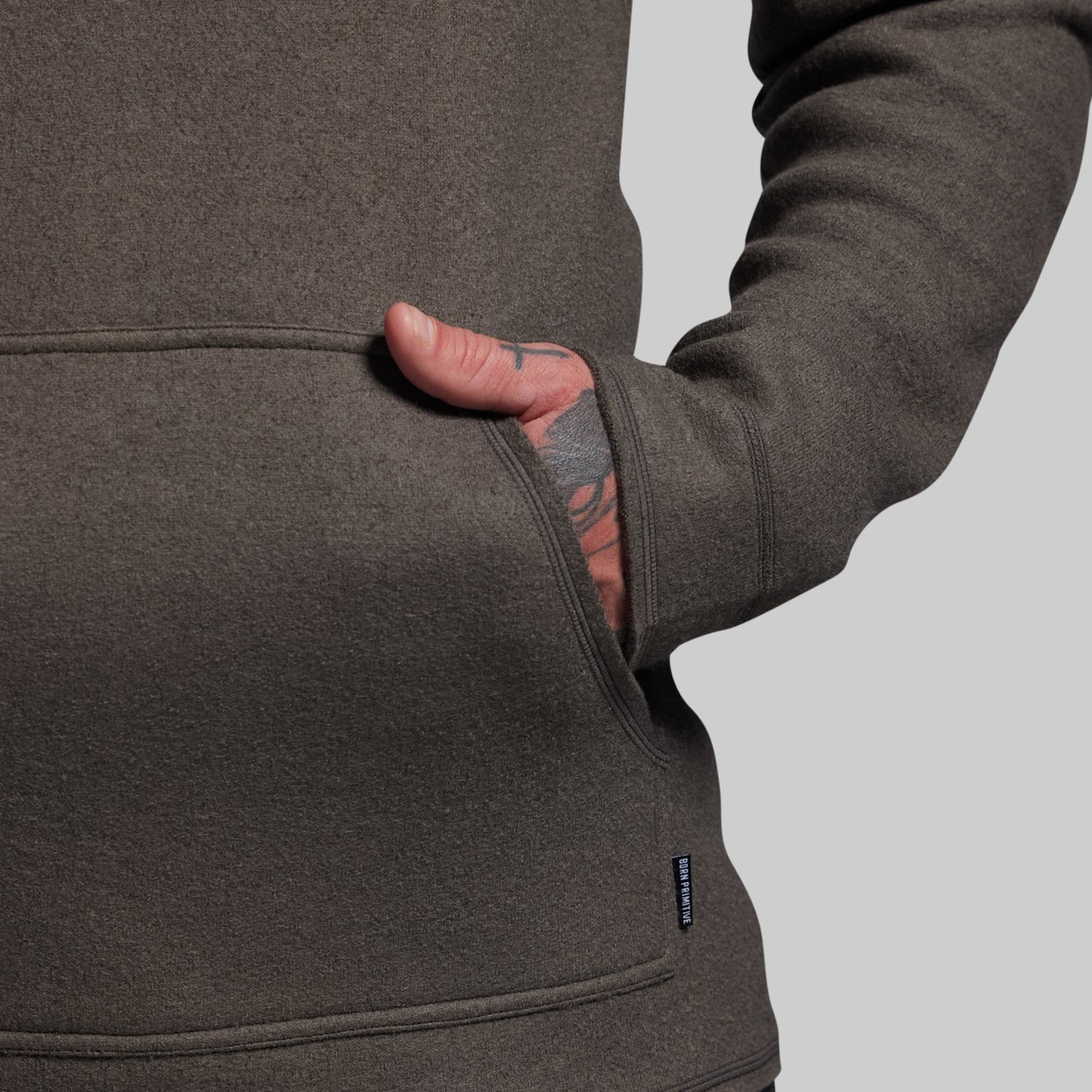 Close-up of a person wearing a gray hoodie with a visible brand logo on a light gray background