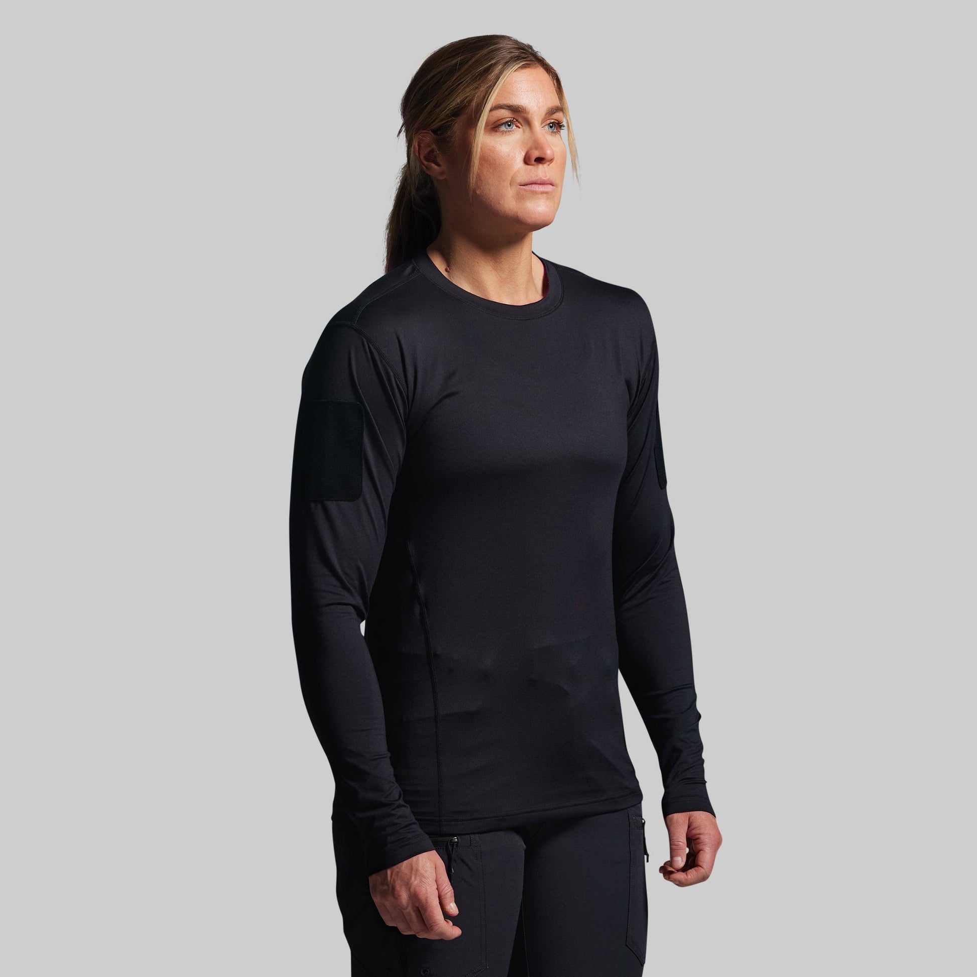 Person wearing a black long-sleeve tactical shirt on a gray background