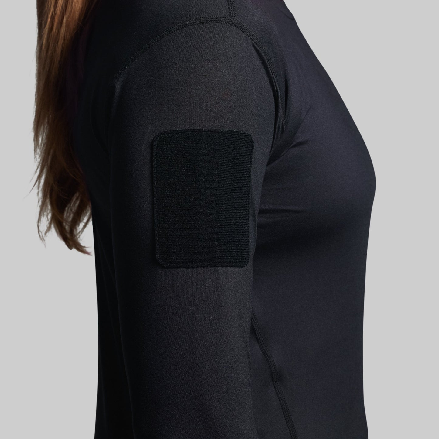 Person wearing a black long-sleeve shirt with a velcro patch on a gray background