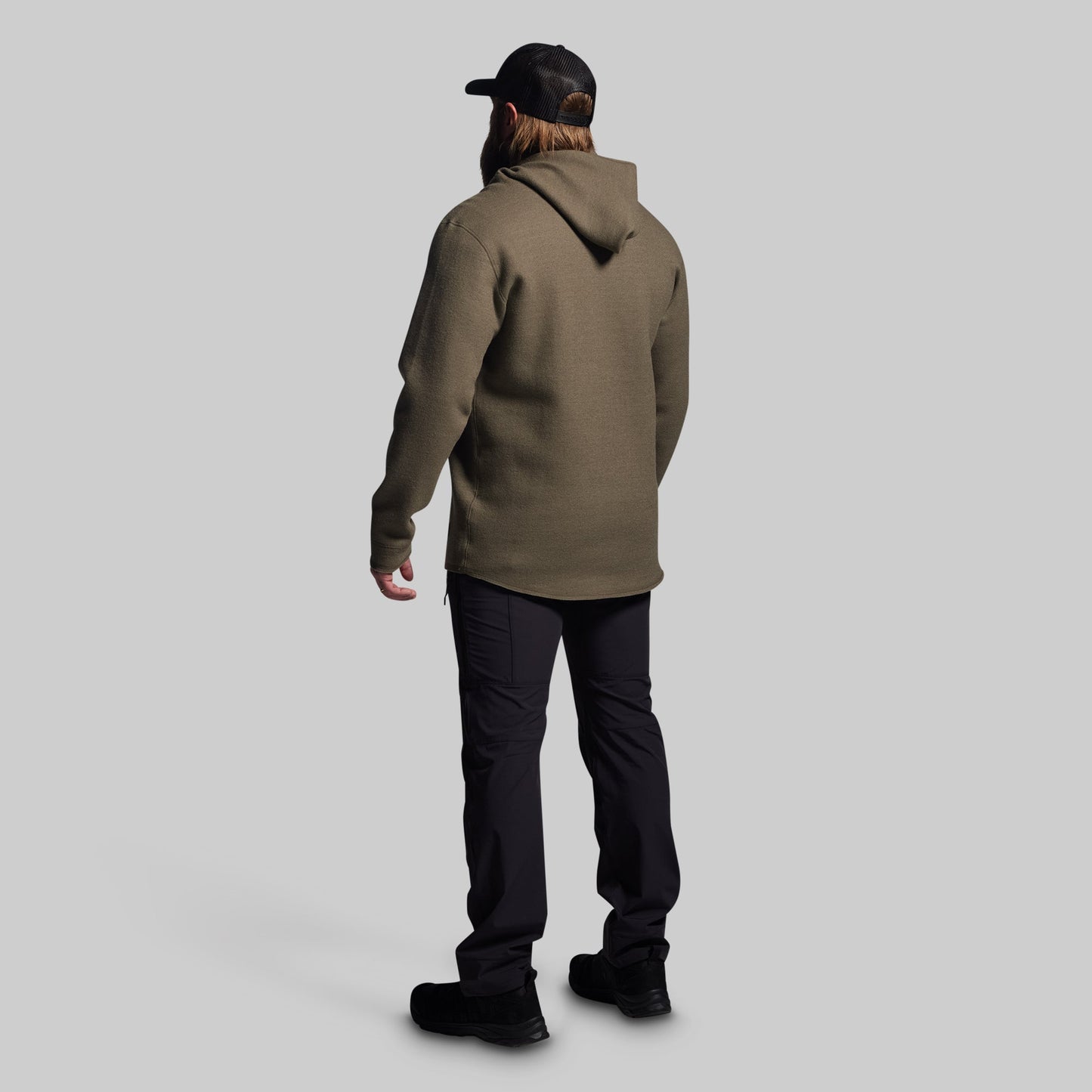 Person wearing a green hoodie and black pants on a light gray background