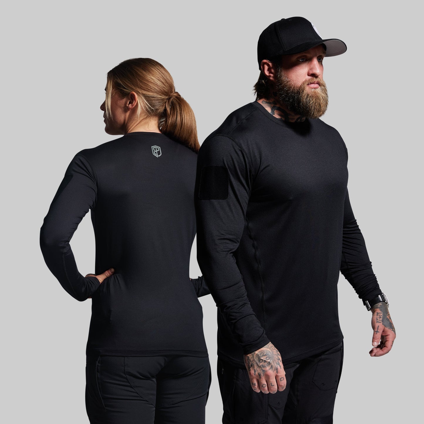 Two people wearing black long-sleeve shirts against a gray background