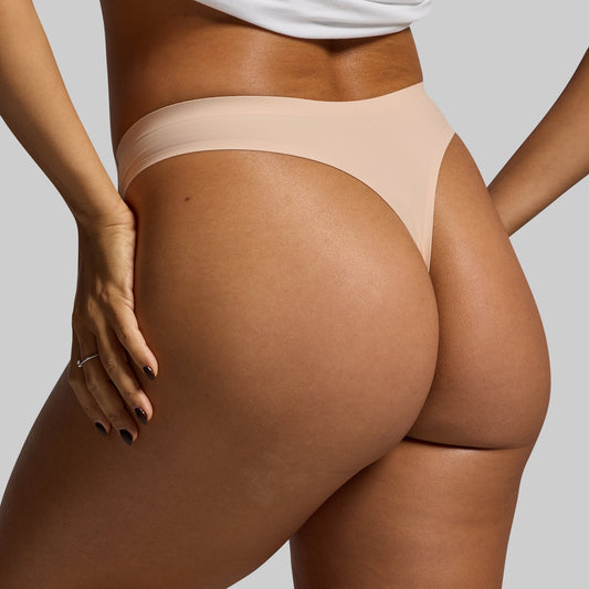 Beige thong underwear worn by a person on a plain background