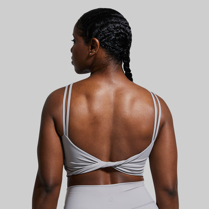 Woman wearing a gray sports bra and leggings on a plain background