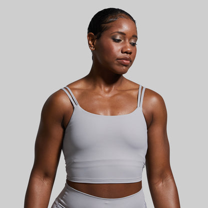 Woman wearing a gray sports bra and leggings against a plain background