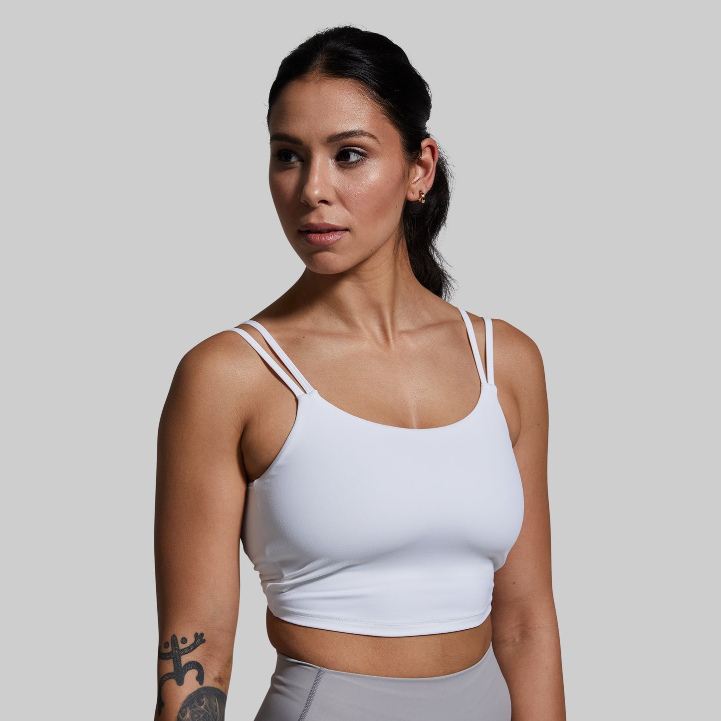 Woman wearing a white sports bra and gray leggings against a plain background