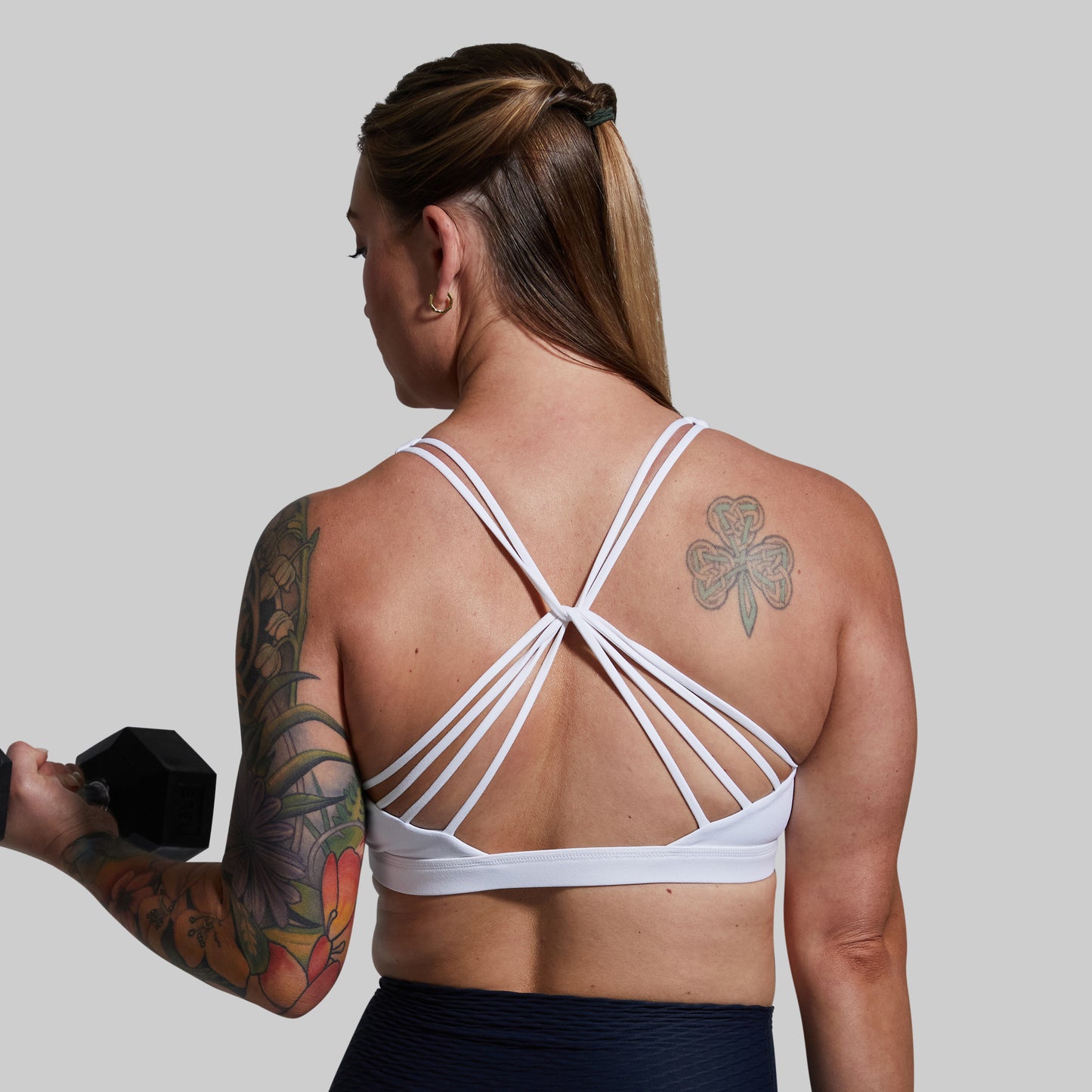 Person wearing a white sports bra holding a dumbbell against a plain background