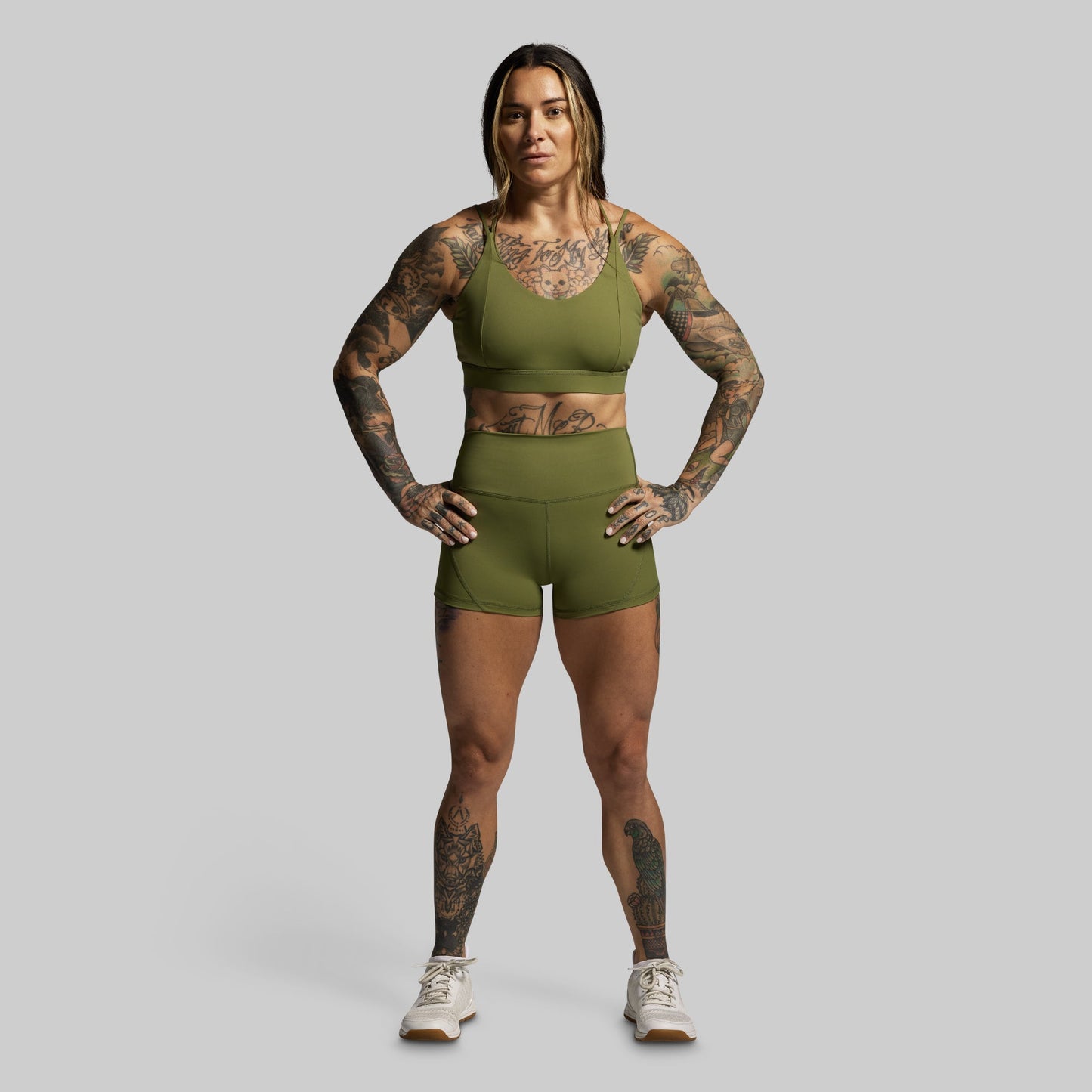 Woman wearing a green athletic outfit with tattoos on a gray background