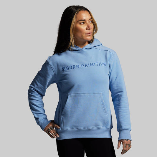 Person wearing a blue hoodie with 'Born Primitive' logo on a gray background