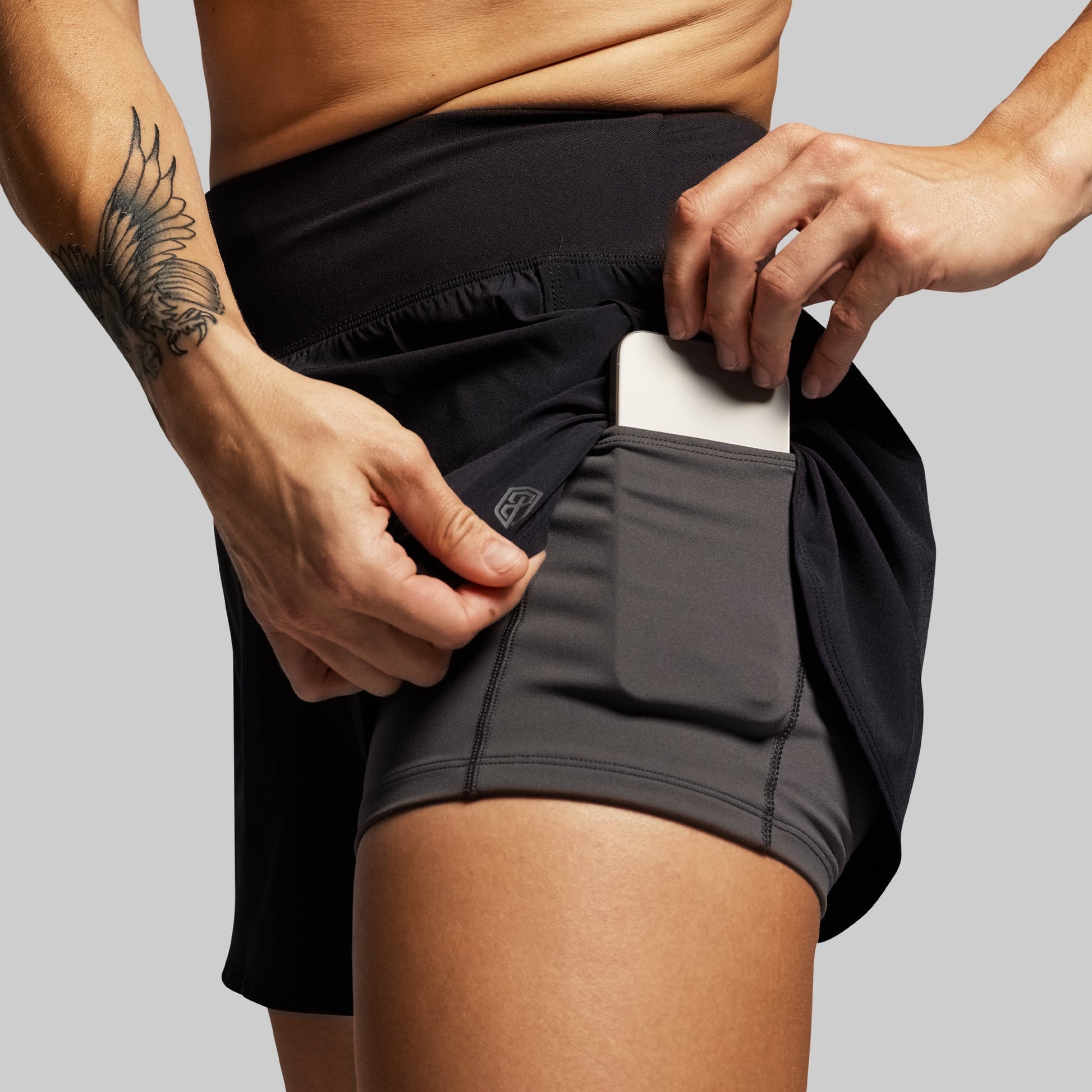 Person wearing black athletic shorts with a pocket, holding a phone.