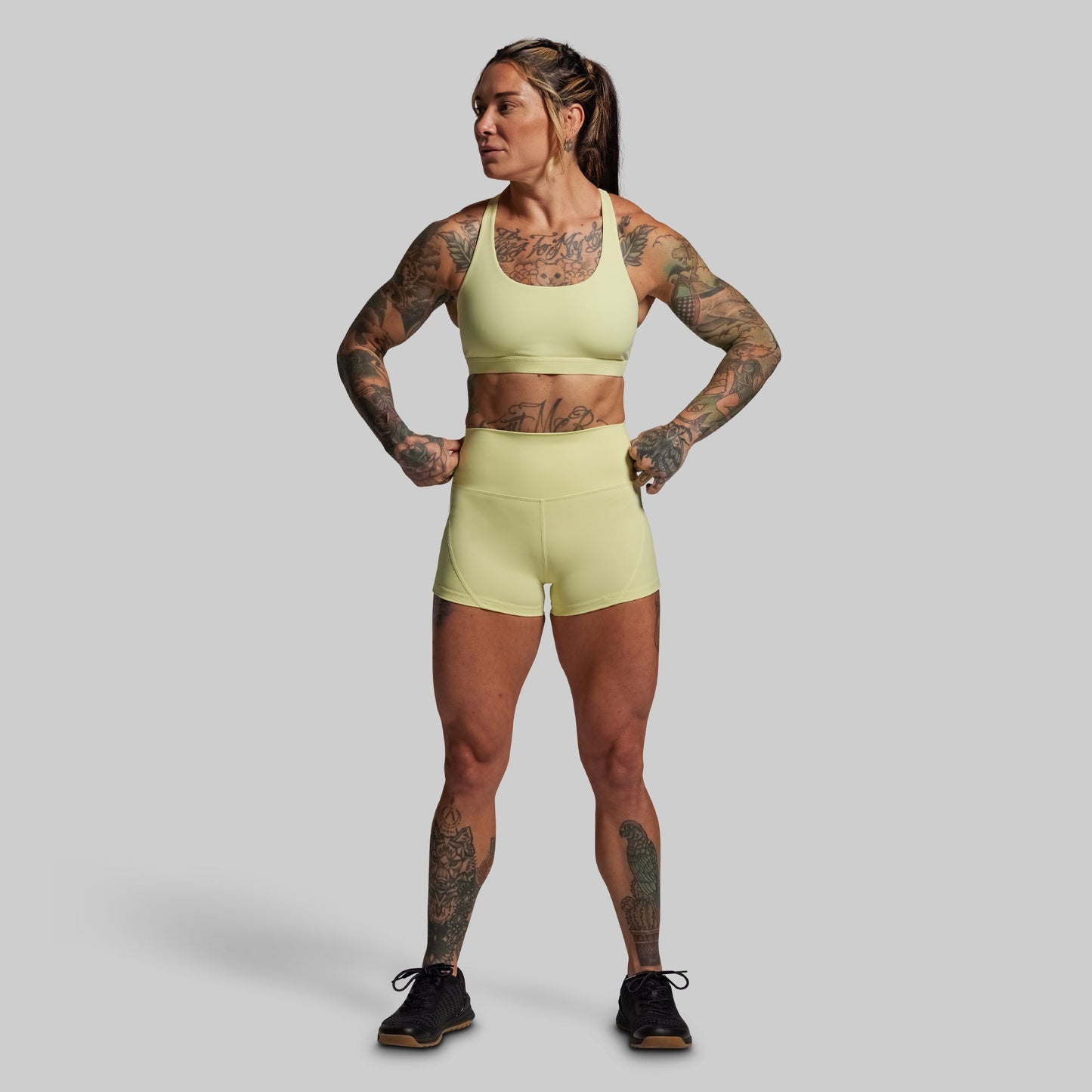 Woman wearing a light yellow athletic outfit with tattoos on a gray background
