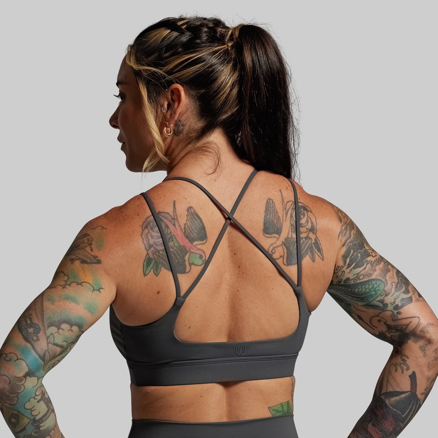 Person wearing a grey sports bra with tattoos on a plain background