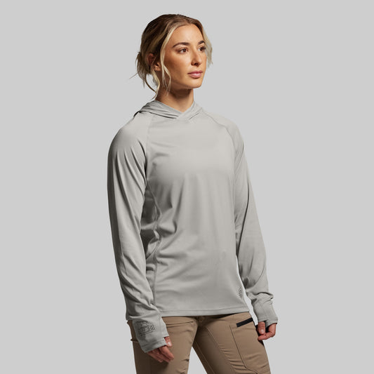 Woman wearing a gray long-sleeve shirt with a hood against a plain background