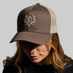 Person wearing a brown and beige cap with a logo on a gray background
