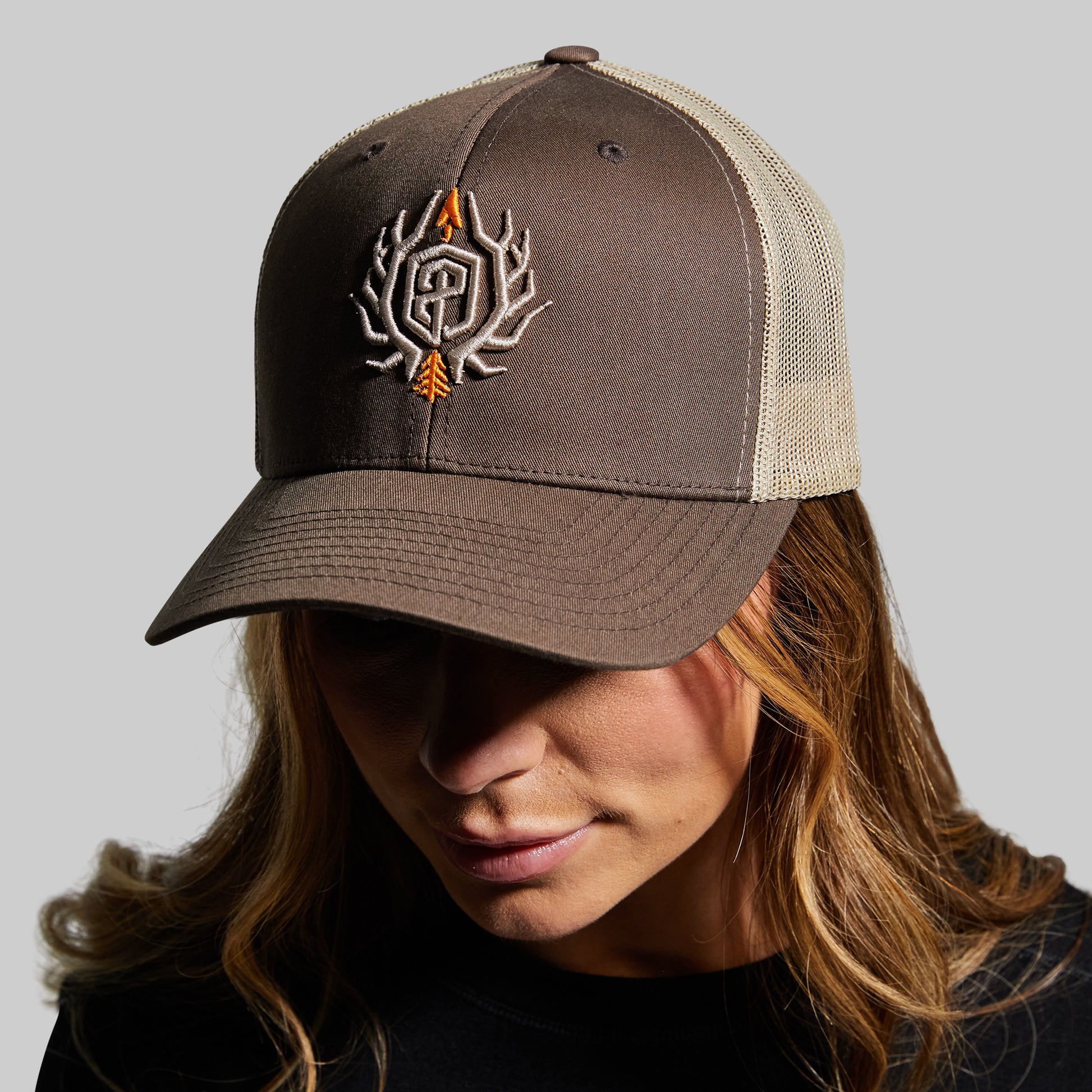 Person wearing a brown and beige cap with a logo on a gray background