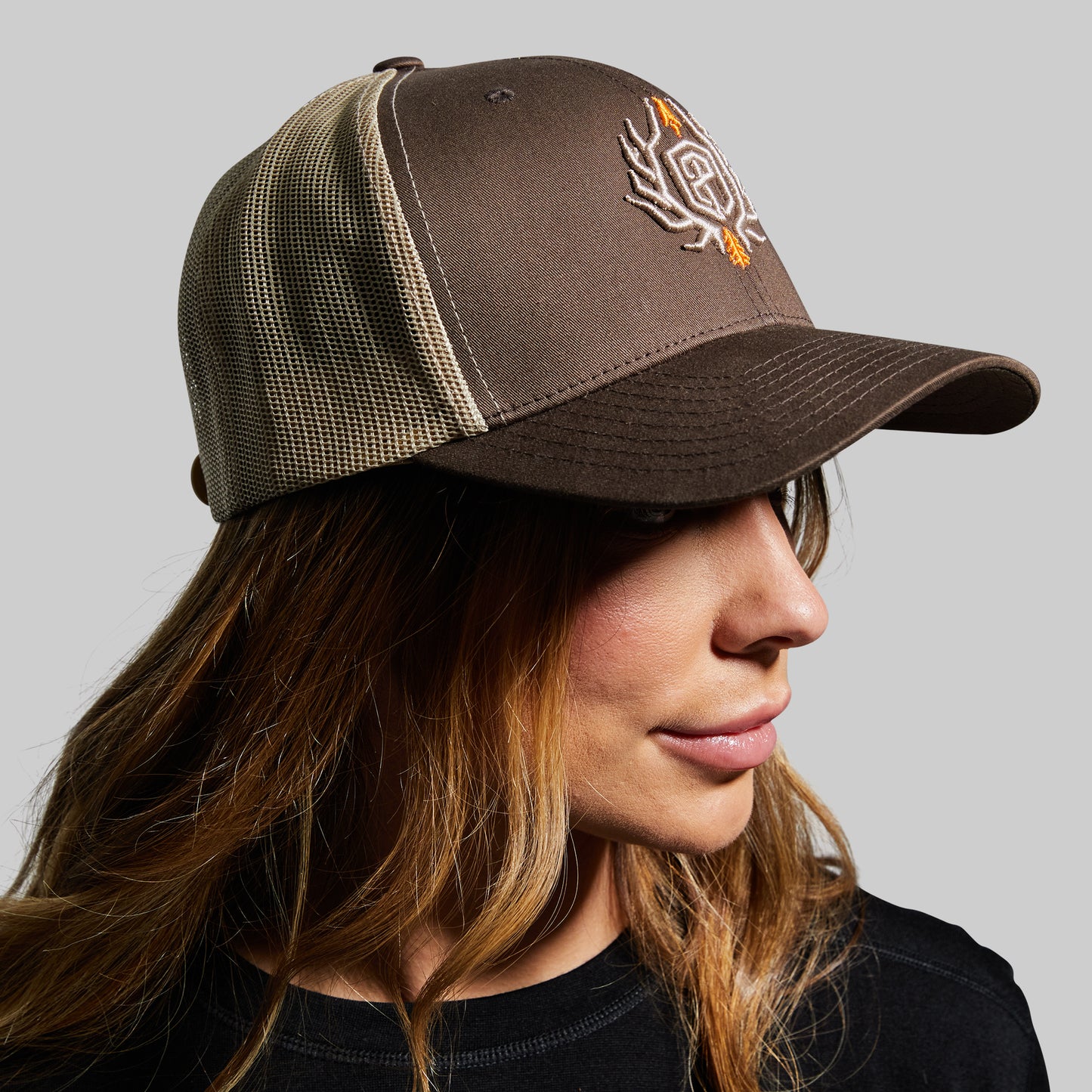 Person wearing a brown and beige cap with a logo on a gray background