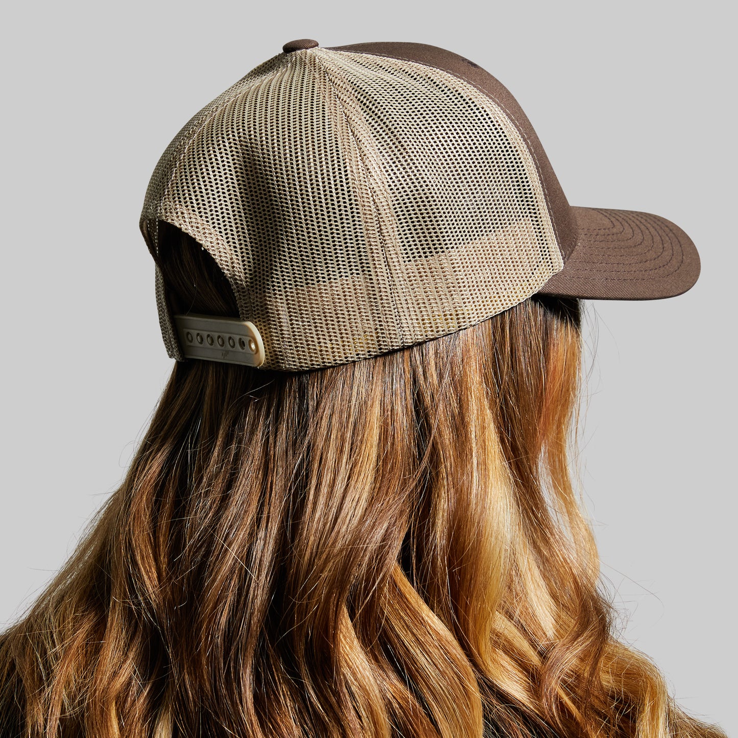 Person wearing a brown and beige mesh cap on a gray background