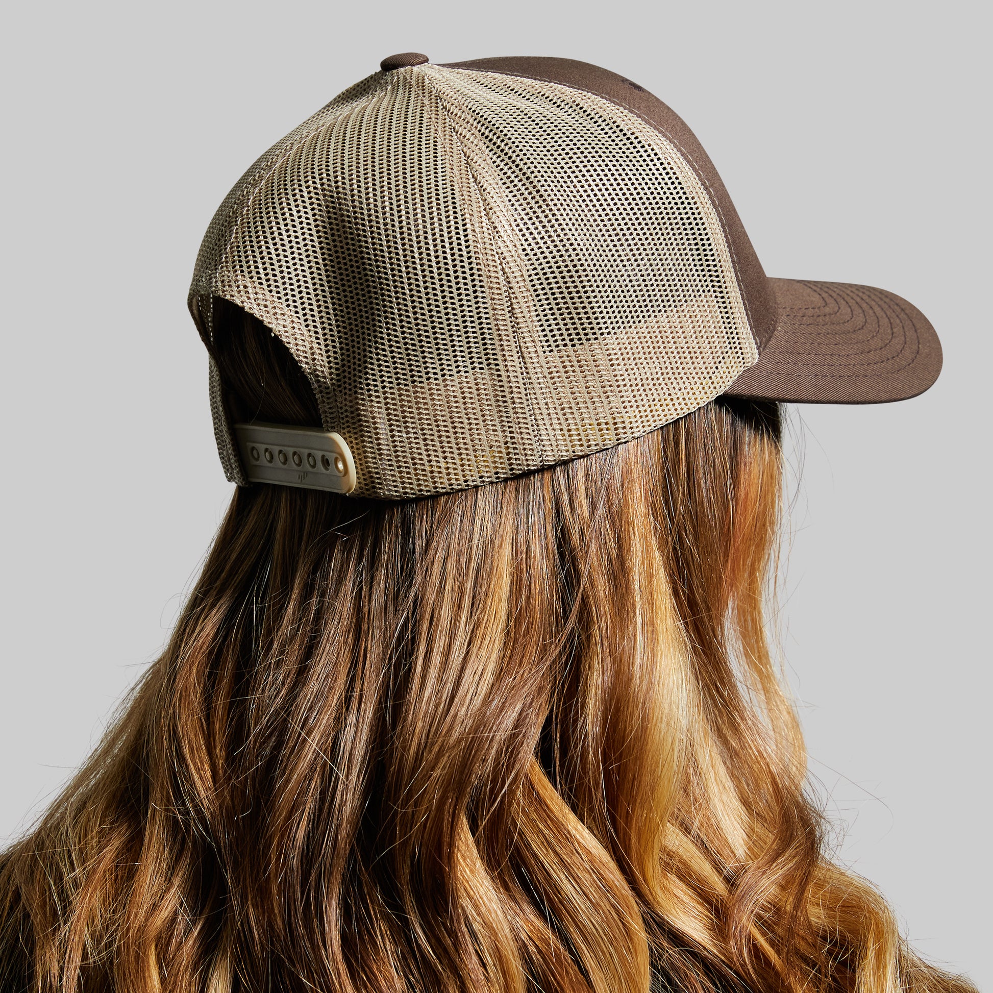 Person wearing a brown and beige mesh cap on a gray background