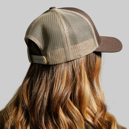 Person wearing a brown and beige mesh cap on a gray background