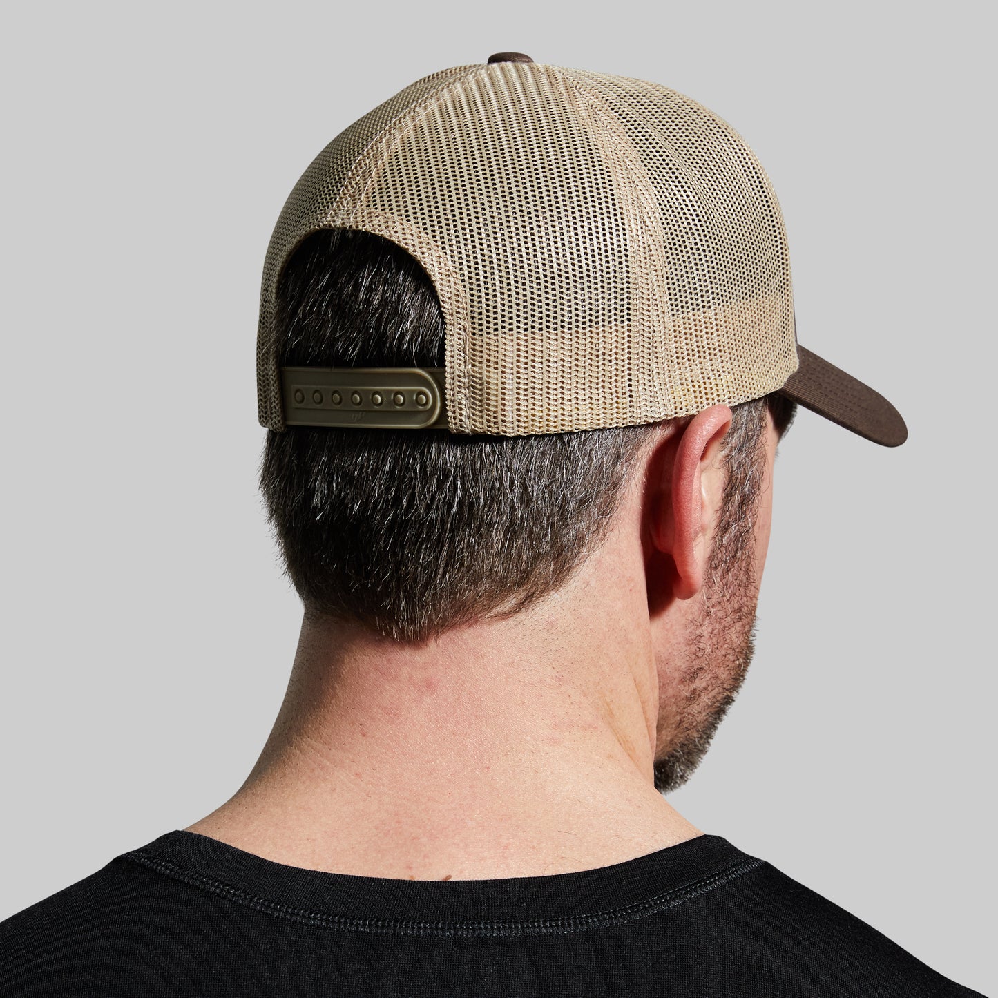 Person wearing a beige mesh cap on a gray background