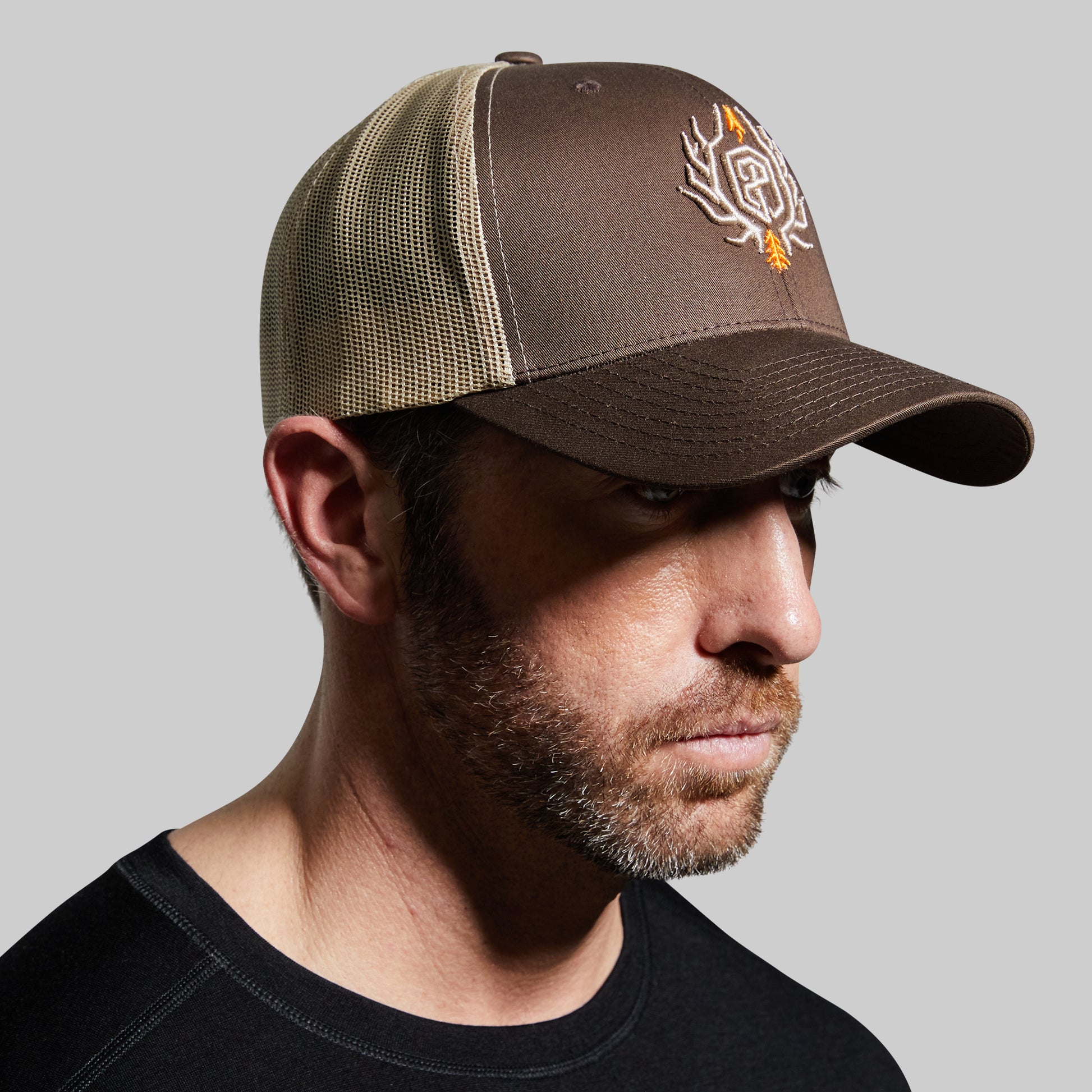 Man wearing a brown and beige cap with a logo on a gray background
