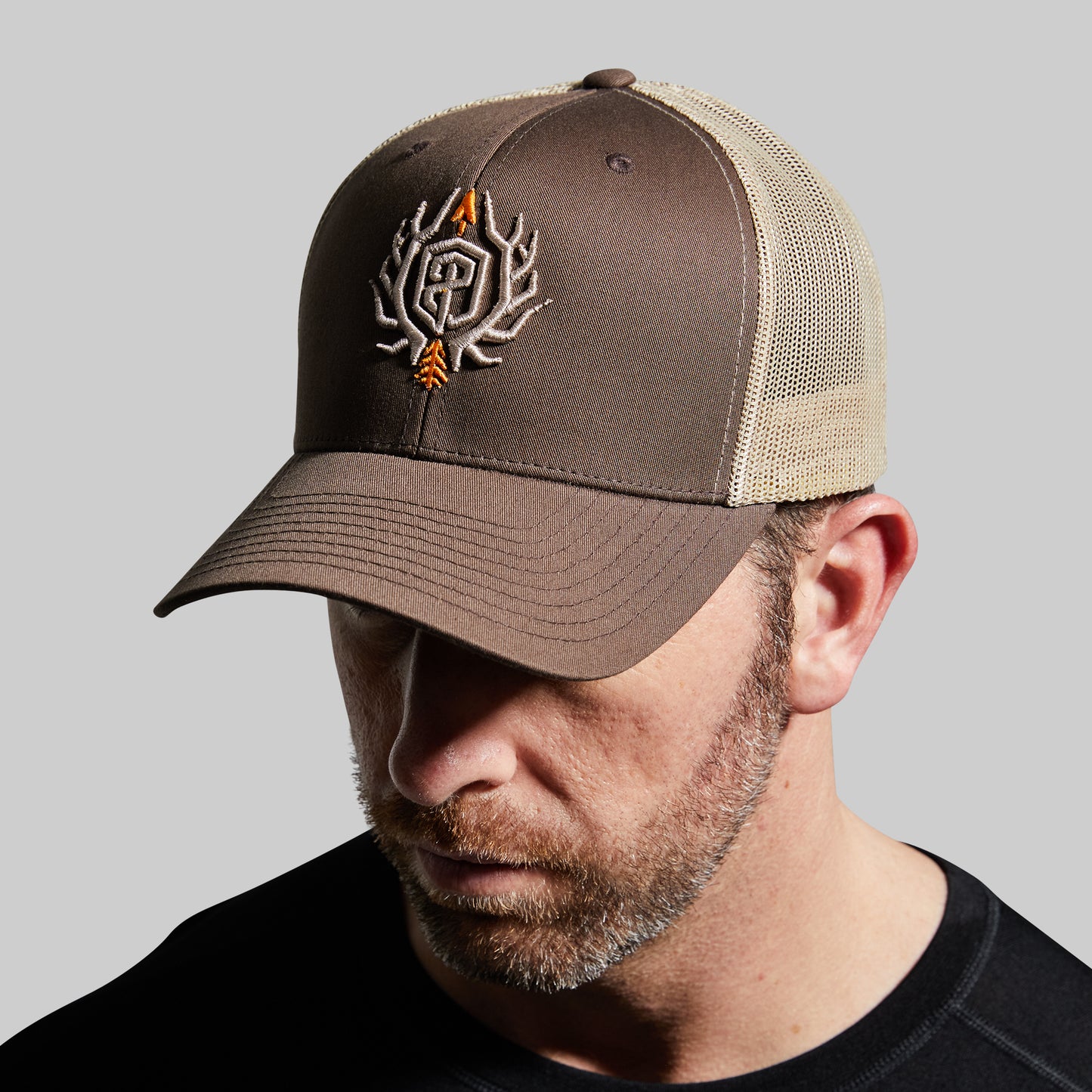 Man wearing a brown and beige cap with a logo on a gray background