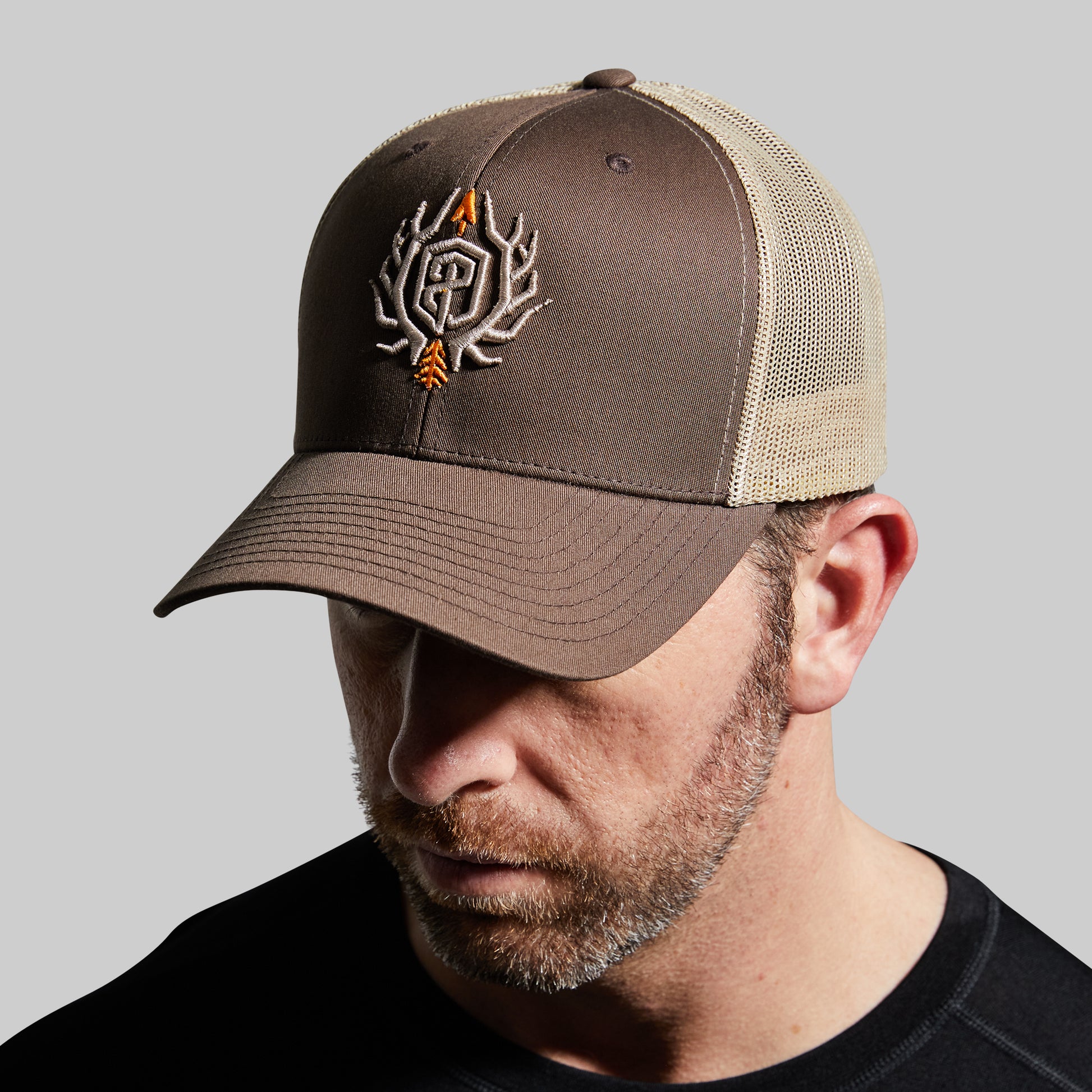 Man wearing a brown and beige cap with a logo on a gray background