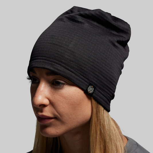 Woman wearing a black beanie with a logo on a gray background